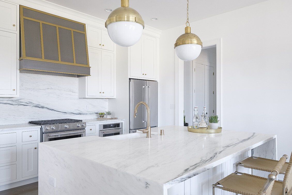 Bright modern kitchen with white marble island, gold pendant lights, white cabinets, and stainless steel appliances