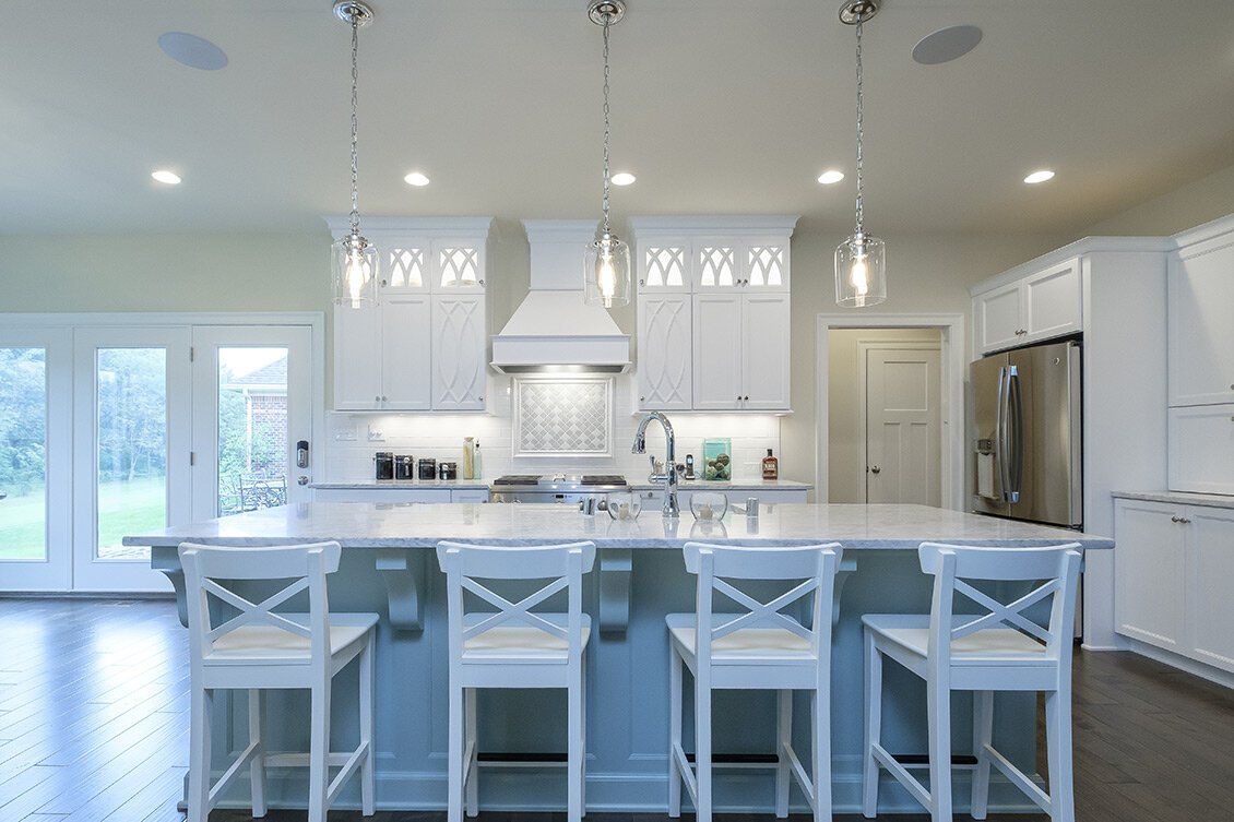 Bright white modern kitchen with island, barstools, pendant lights, and stainless steel appliances