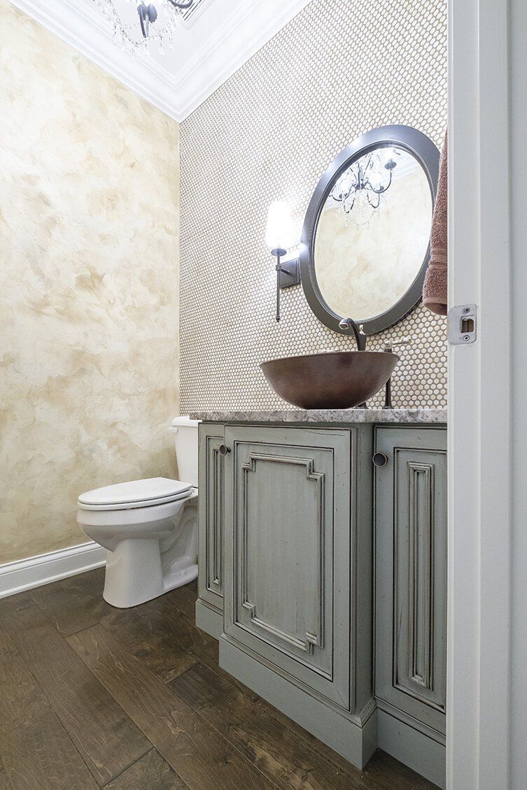 Small bathroom with toilet, patterned tile wall, and vintage vanity with round mirror and bowl sink.