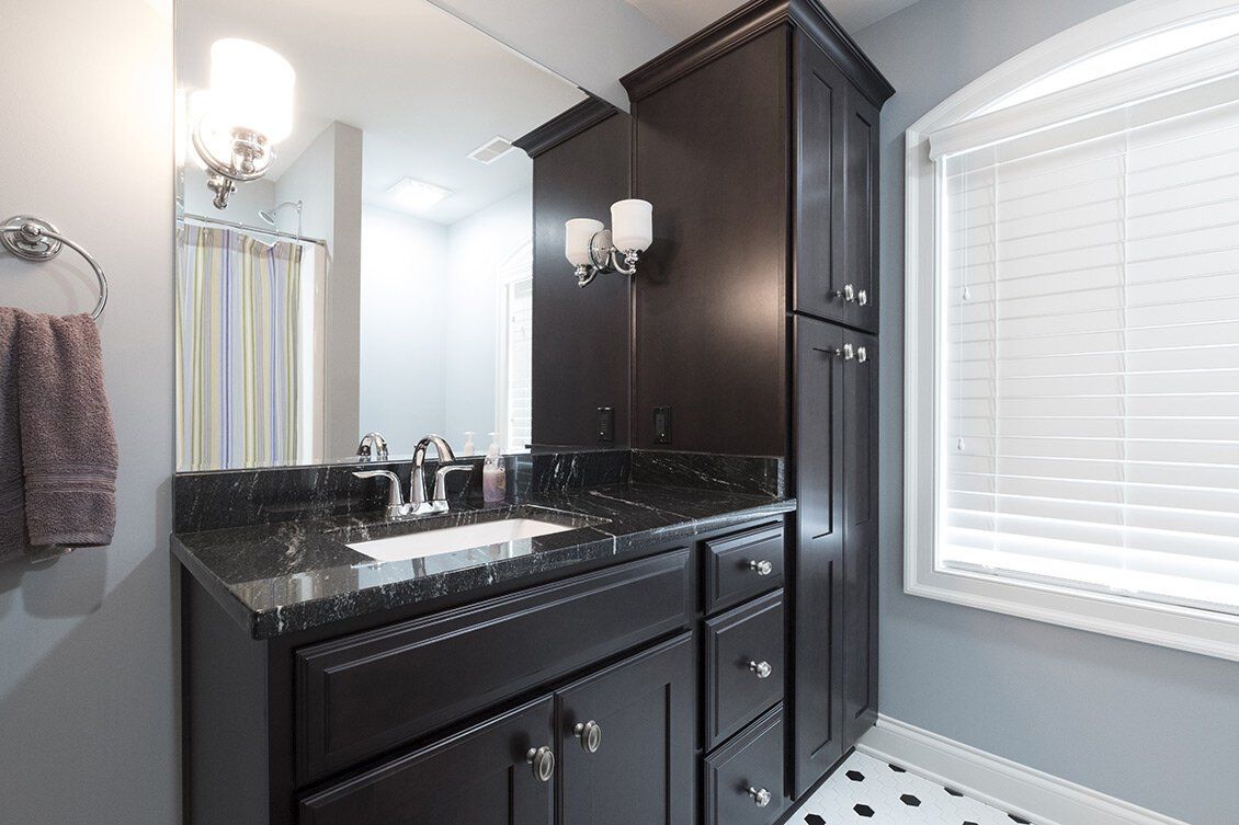 Modern bathroom with dark wood vanity, black countertop, mirror, and window blinds