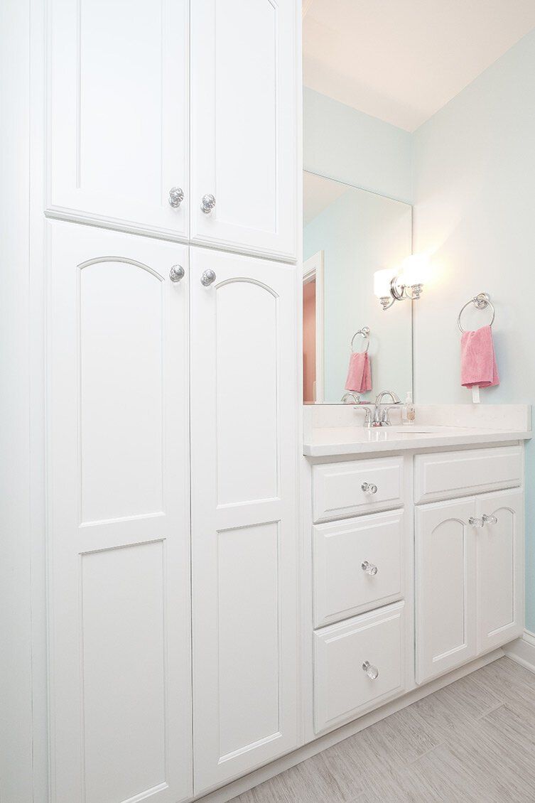 Bright white bathroom vanity and tall cabinet with sink, mirror, pink towels, and gray floor tiles