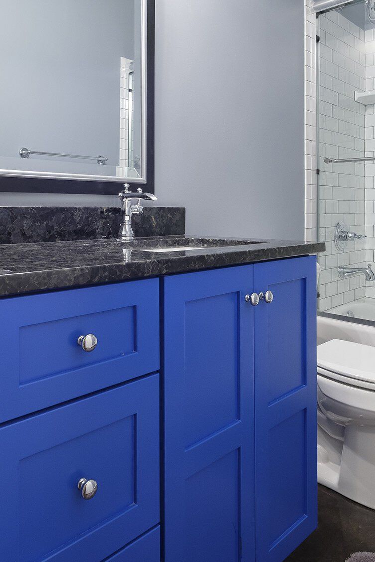 Blue bathroom vanity with black countertop, mirror, sink faucet, and a toilet visible beside it.