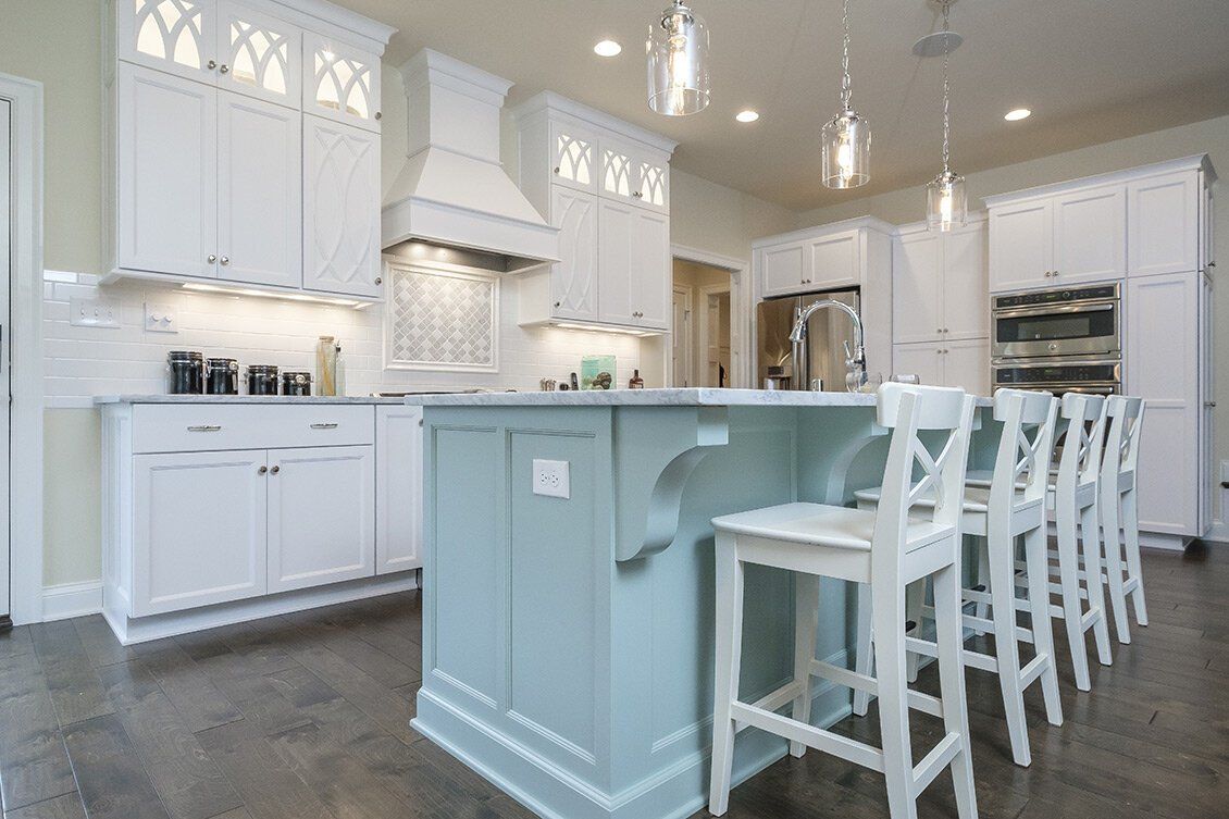 Bright white kitchen with a pale blue island and white bar stools under pendant lights