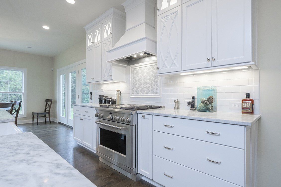 Bright white modern kitchen with stainless steel stove, marble counters, and tiled backsplash