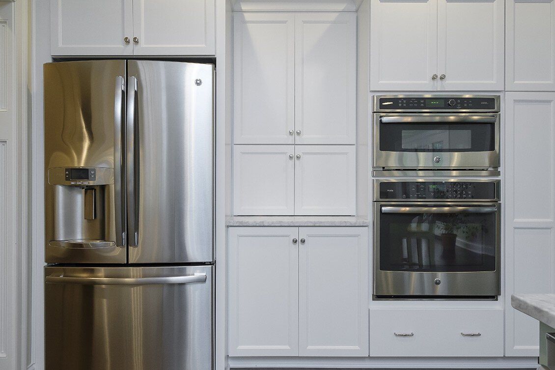 Modern white kitchen with stainless steel refrigerator and built-in double oven cabinets
