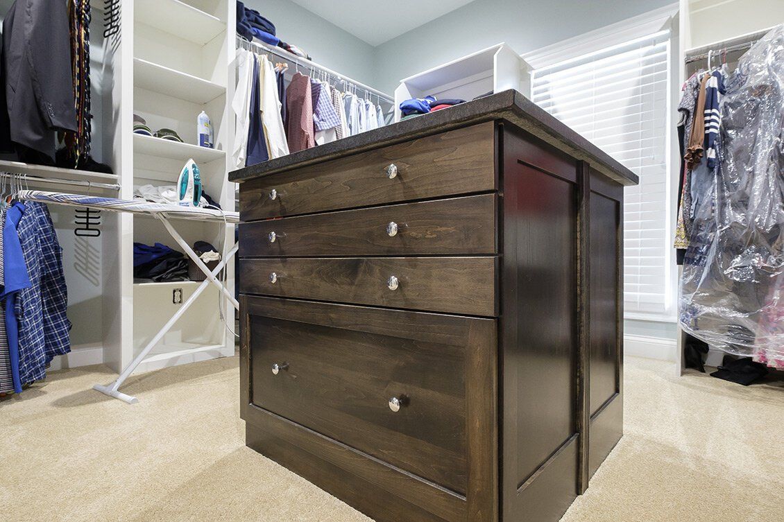 Dark wood dresser in a beige walk-in closet with clothes hanging on both sides.