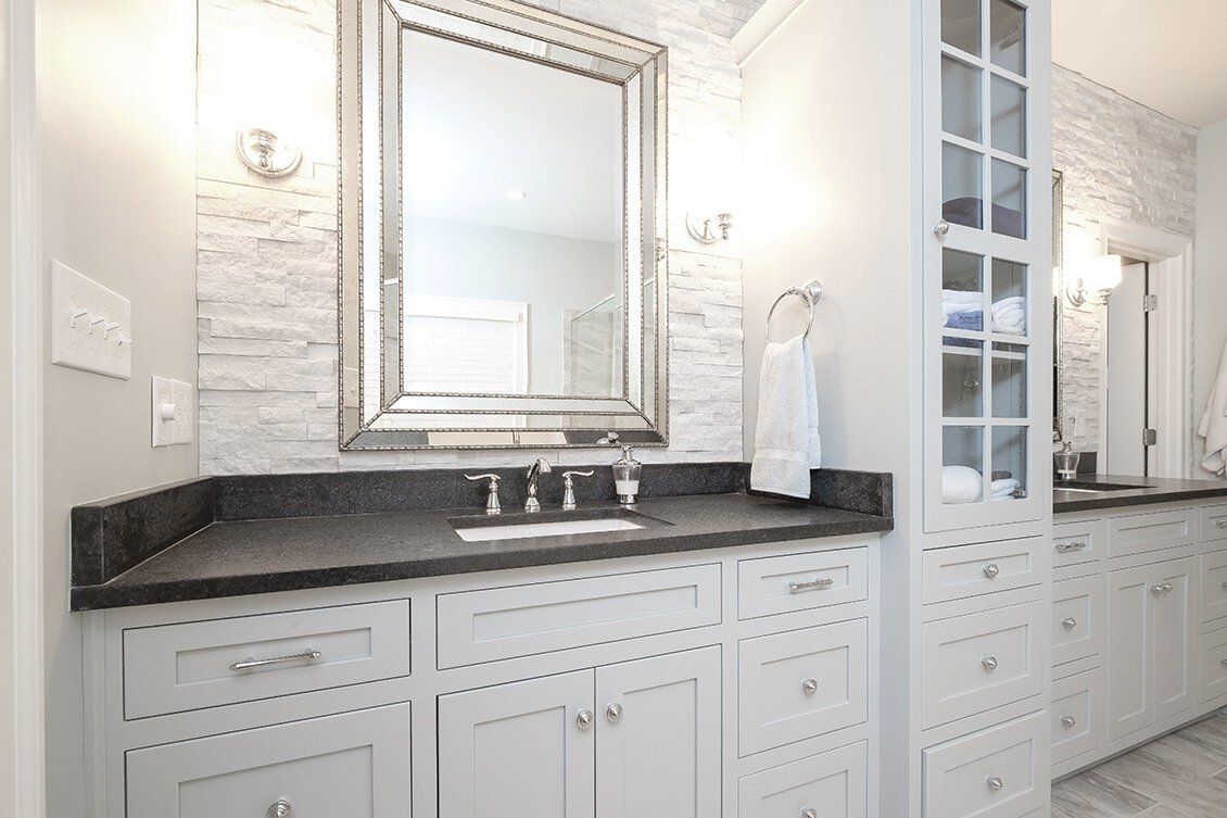Bright white bathroom vanity with dark countertop, mirror, and double sinks in a tiled interior.