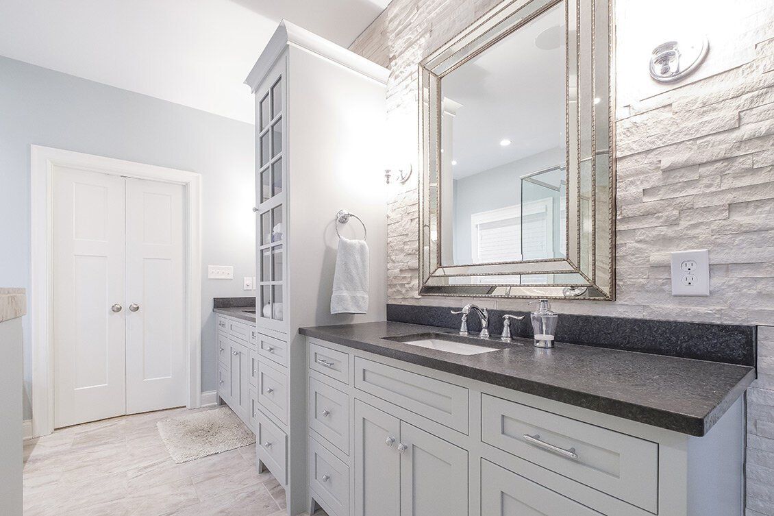 Bright bathroom with white cabinets, dark countertop, large mirror, and stone accent wall.