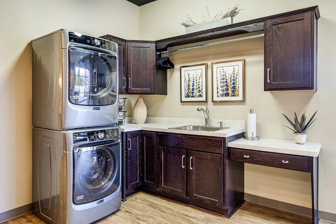 Laundry room with stacked washer and dryer, dark wood cabinets, and built-in counter sink