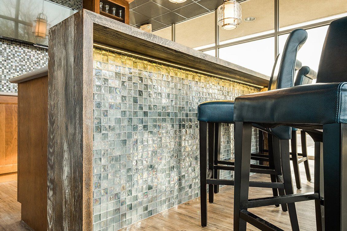 Bar with mosaic tile front, wooden counter, and tall stools in a modern interior