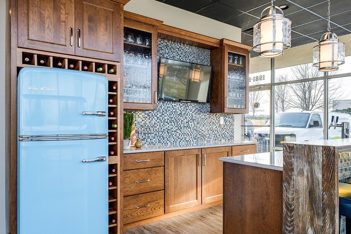 Modern kitchen with light blue retro fridge, wood cabinets, mosaic backsplash, and a large window.