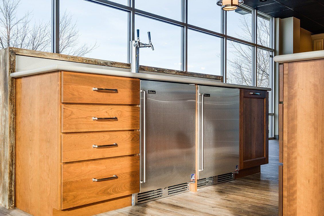 Modern kitchen island with stainless steel cabinets, wooden drawers, and large windows above a stone floor
