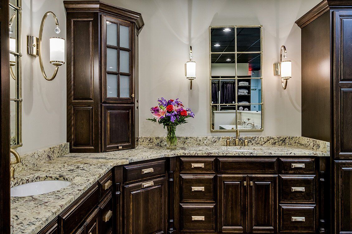 Dark wood bathroom vanity with granite countertop, wall sconces, and a vase of colorful flowers.