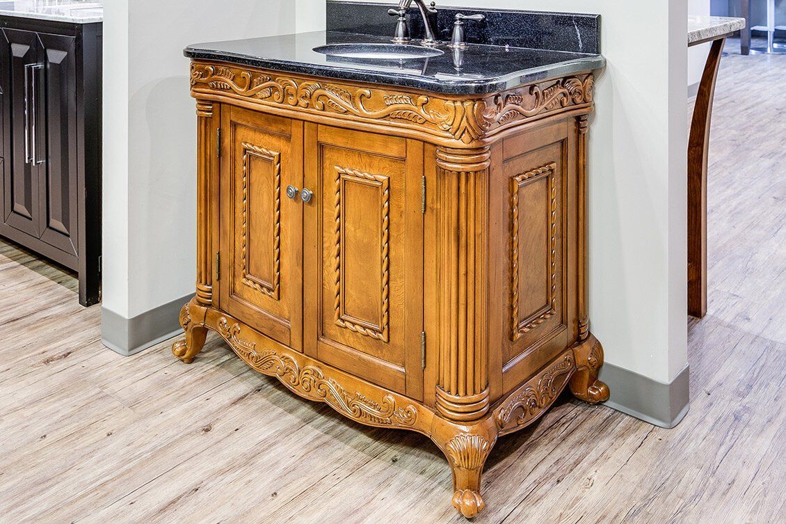 Ornate wooden bathroom vanity with black marble countertop and sink beside a wall