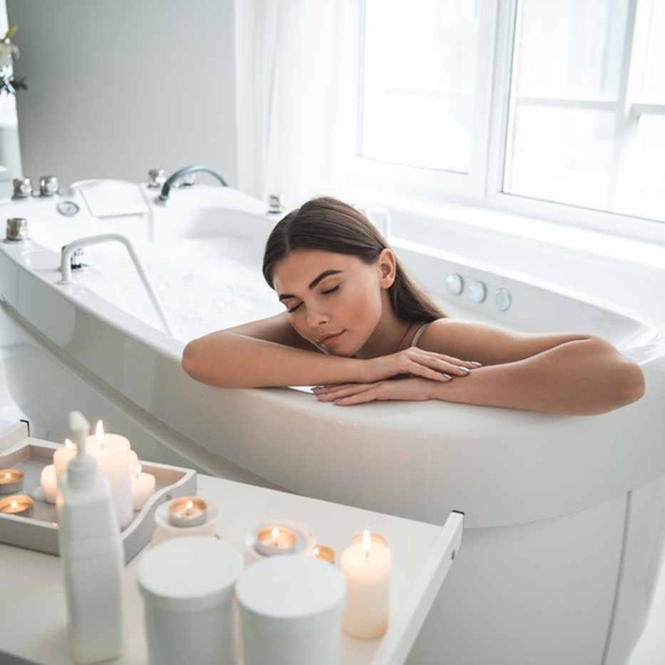 Woman relaxing in a white bathtub with candles in a bright bathroom