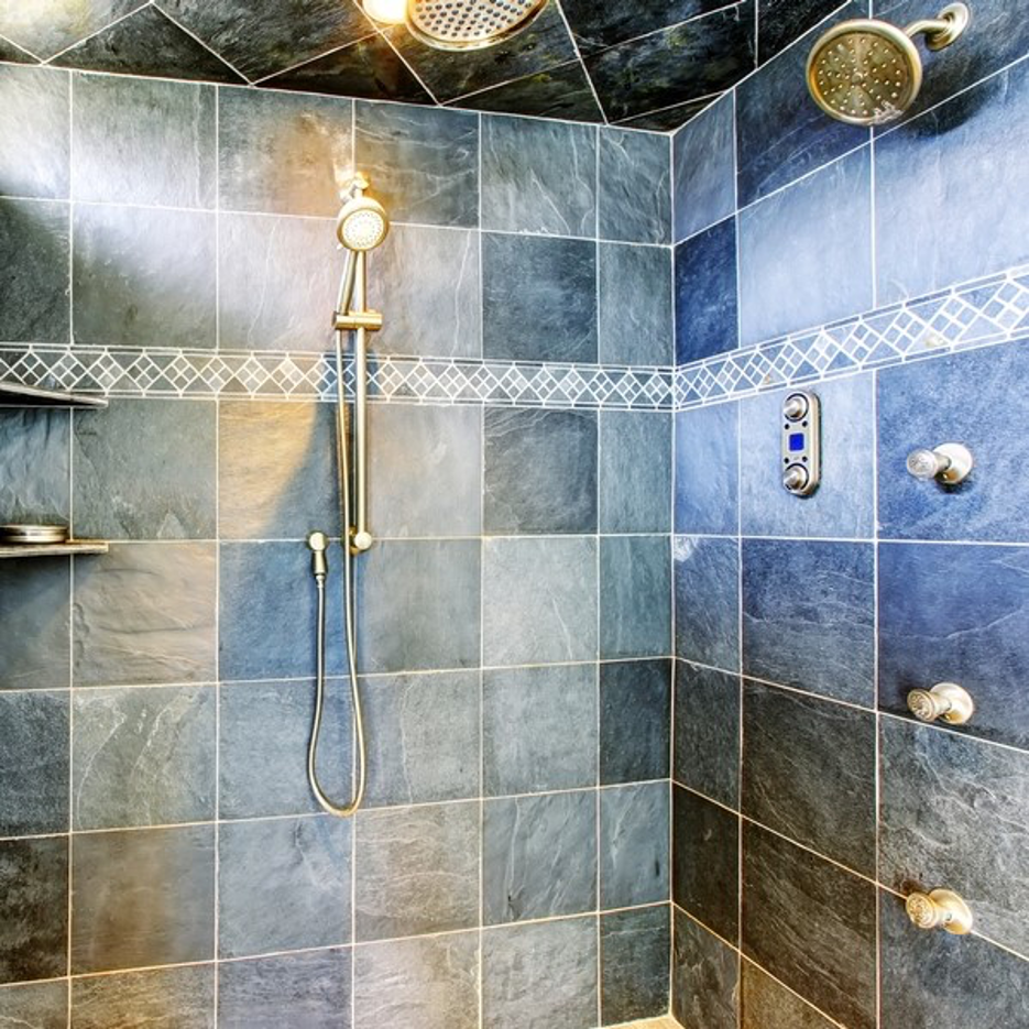 Blue tiled shower with gold fixtures, rainfall head, handheld wand, and wall controls.