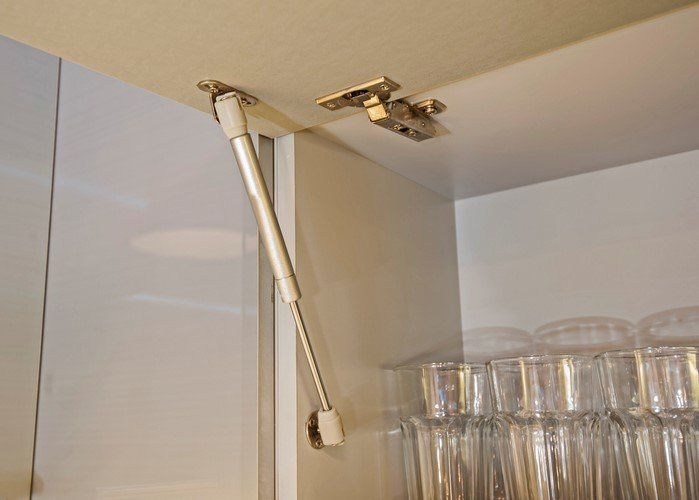 Cabinet door support strut inside a kitchen cabinet above stacked drinking glasses