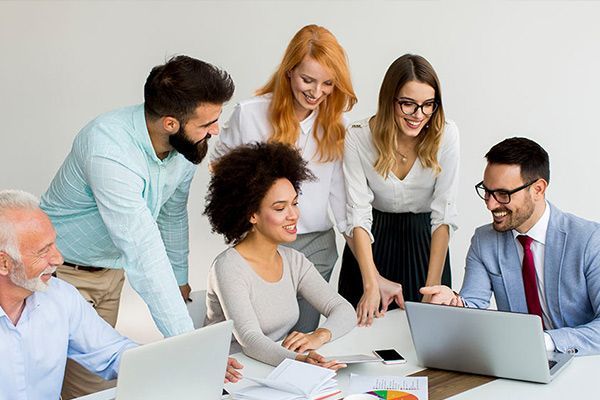 A diverse team of professionals collaborate around a laptop in a bright, modern office setting.