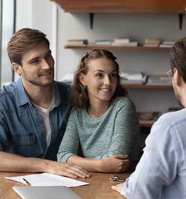 A couple sits at a wooden table across from a consultant, looking toward them with pleasant, attentive expressions.