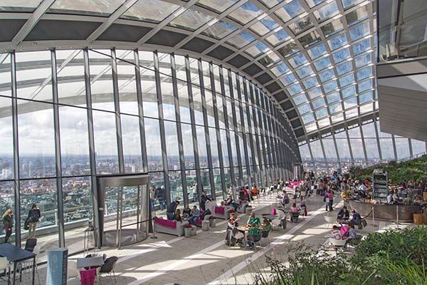 People relax in the Sky Garden, a glass-enclosed observation deck with lush plants and views of the London skyline.