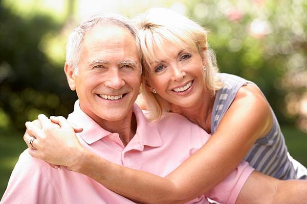 A smiling couple embracing outdoors in a park-like setting.