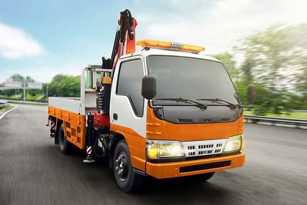 A white and orange service truck with a crane mounted on the back driving along a paved road.