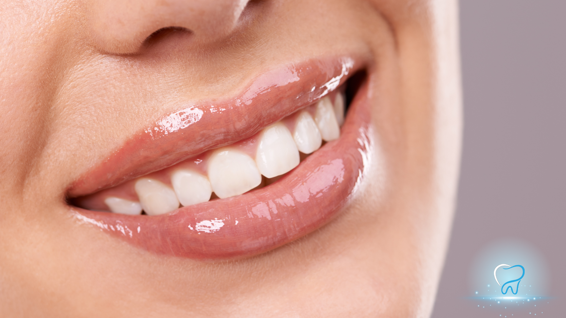 Close-up of a smiling mouth with glossy pink lips and white teeth