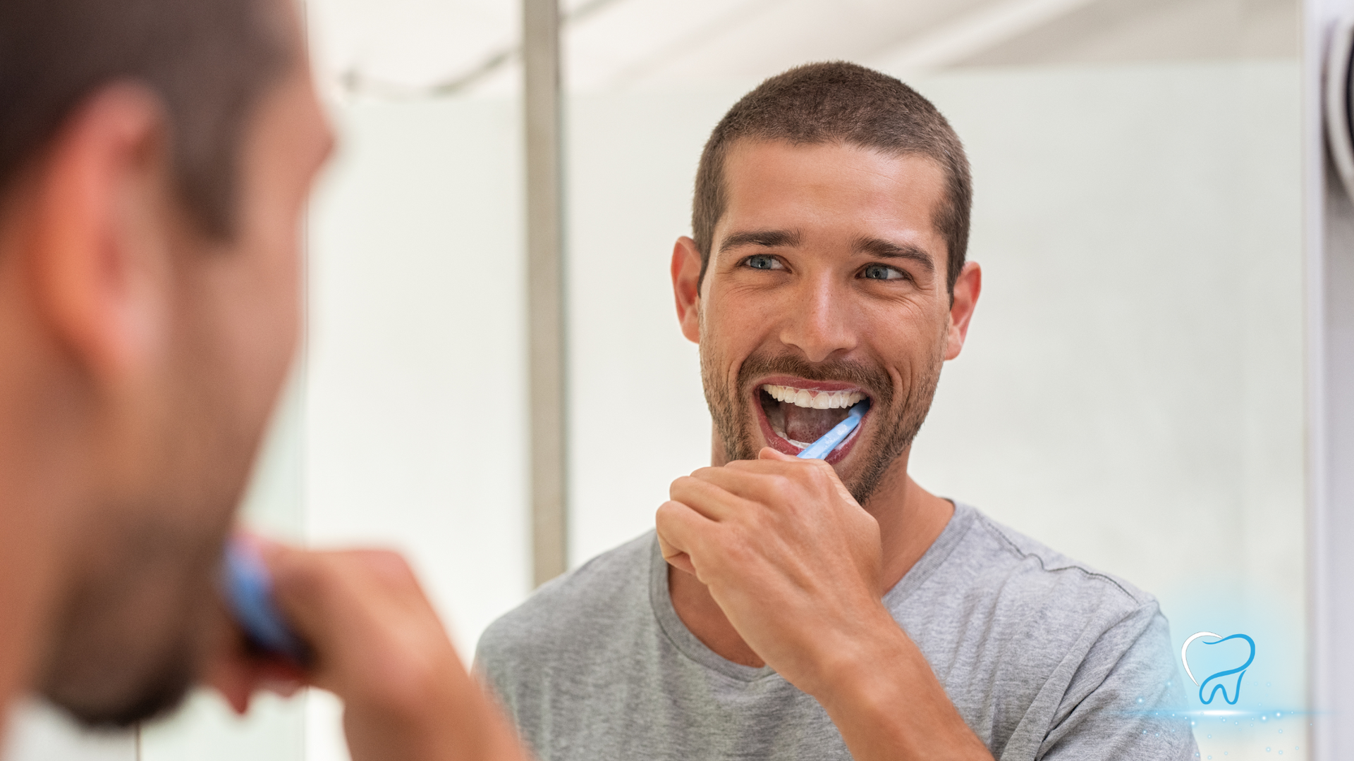 Man brushing teeth in a bathroom mirror, smiling while holding a toothbrush.