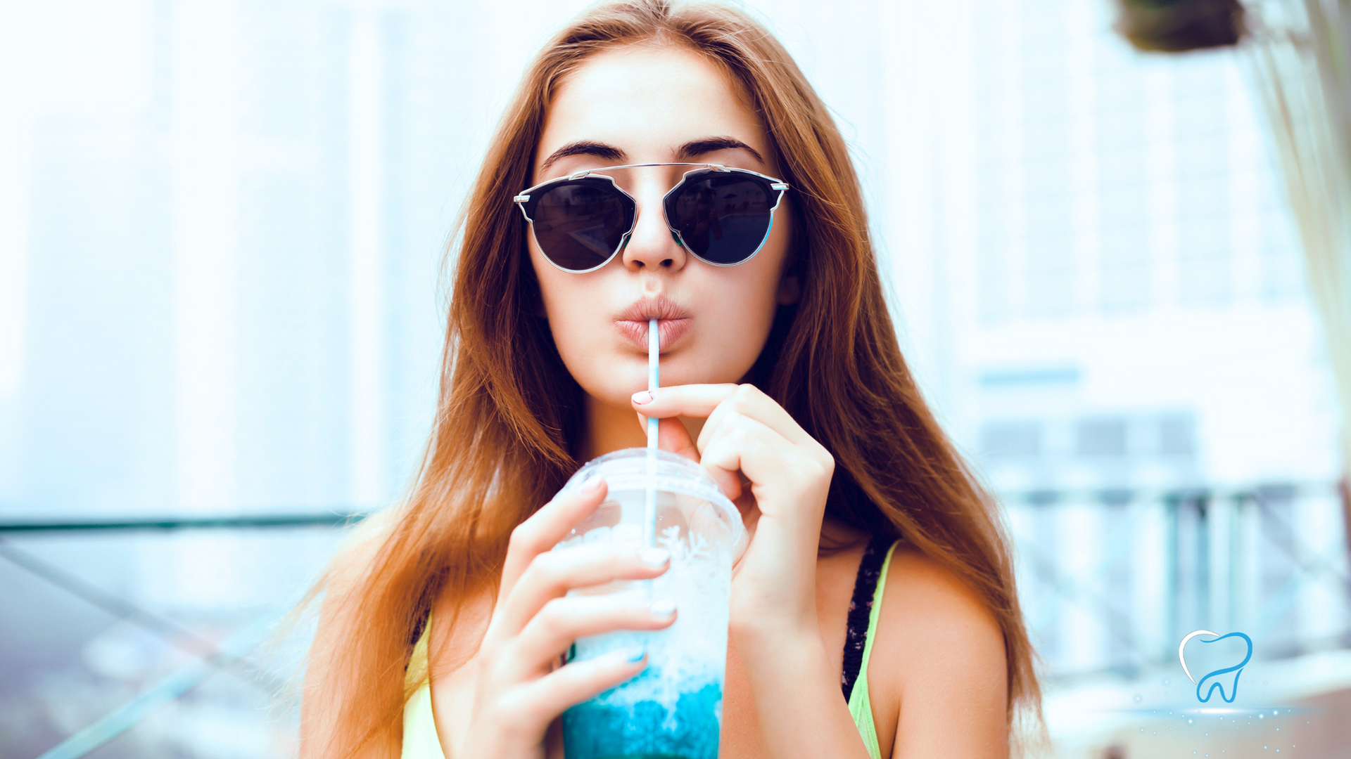 Woman in sunglasses drinking a blue iced beverage with a straw outdoors