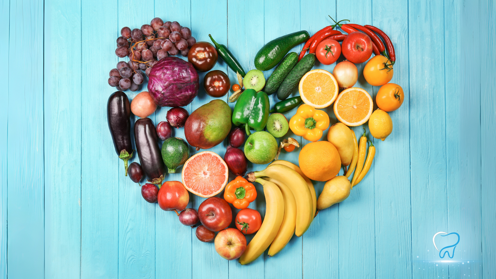 Heart-shaped arrangement of assorted colorful fruits on a light blue wooden background