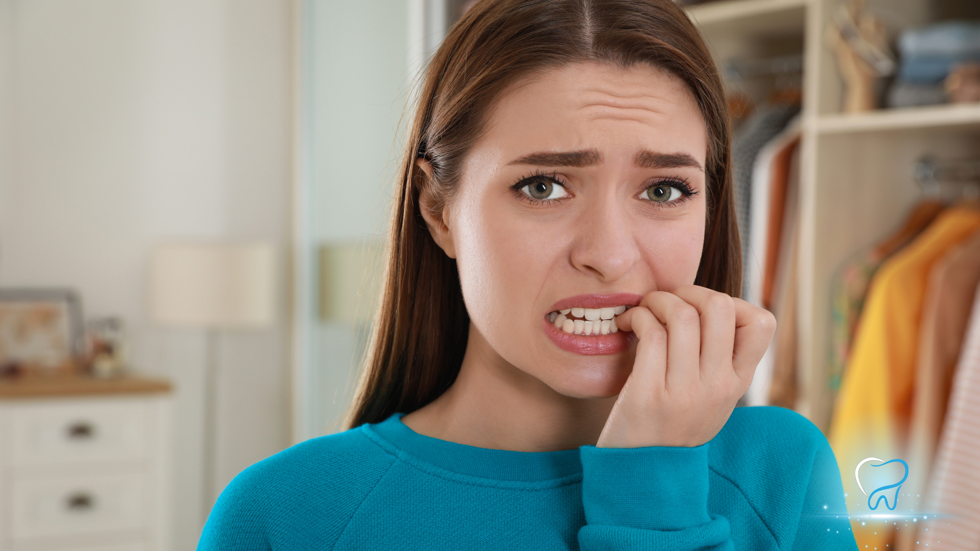 Woman in a blue sweater biting her nails, looking anxious in a bedroom or closet area.