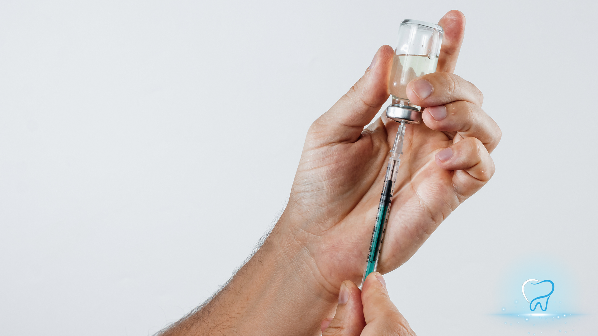 Hand holding a syringe and vaccine vial against a white background