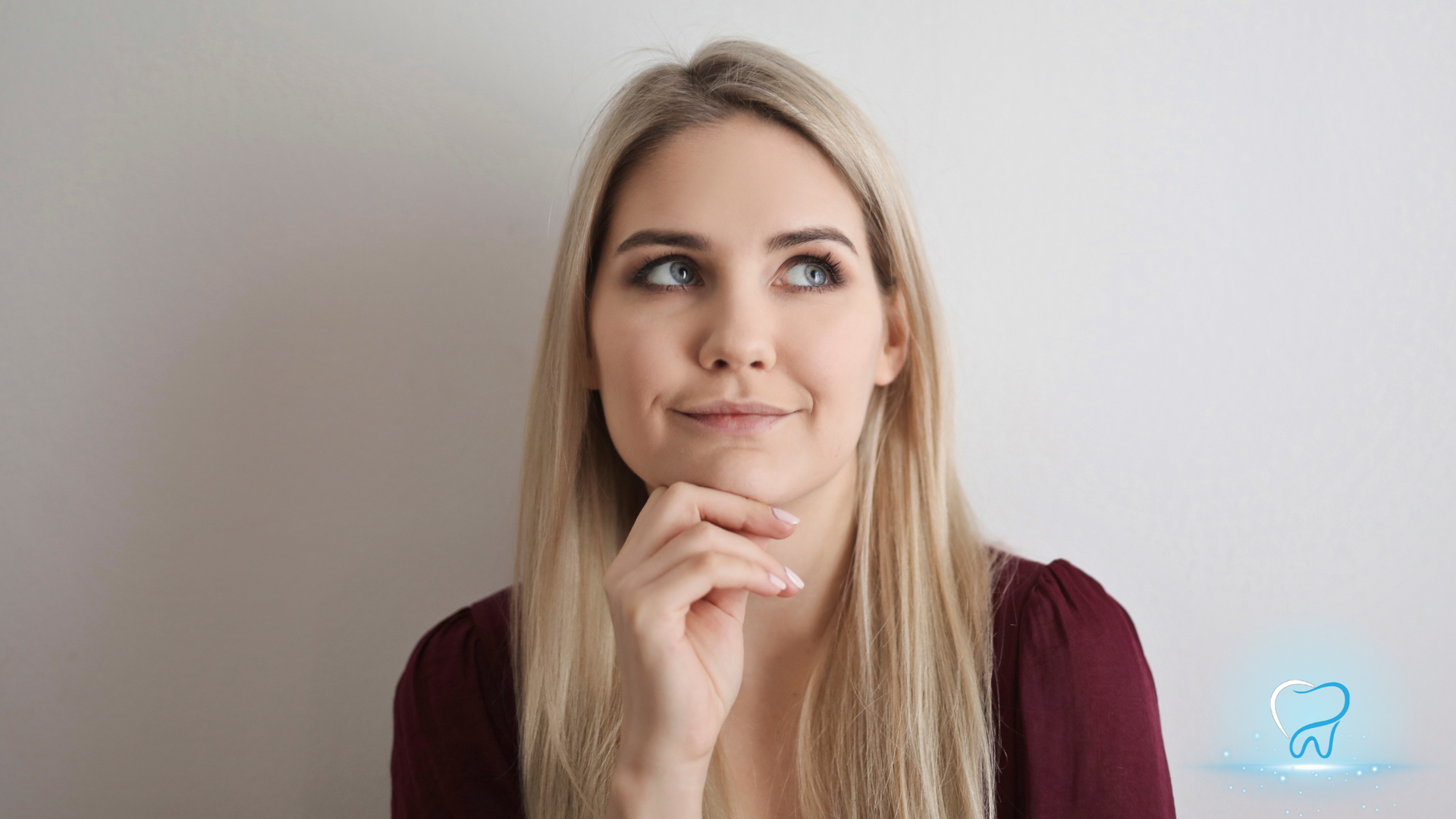Blonde woman in a maroon top resting her chin on her hand, looking thoughtfully to the side.