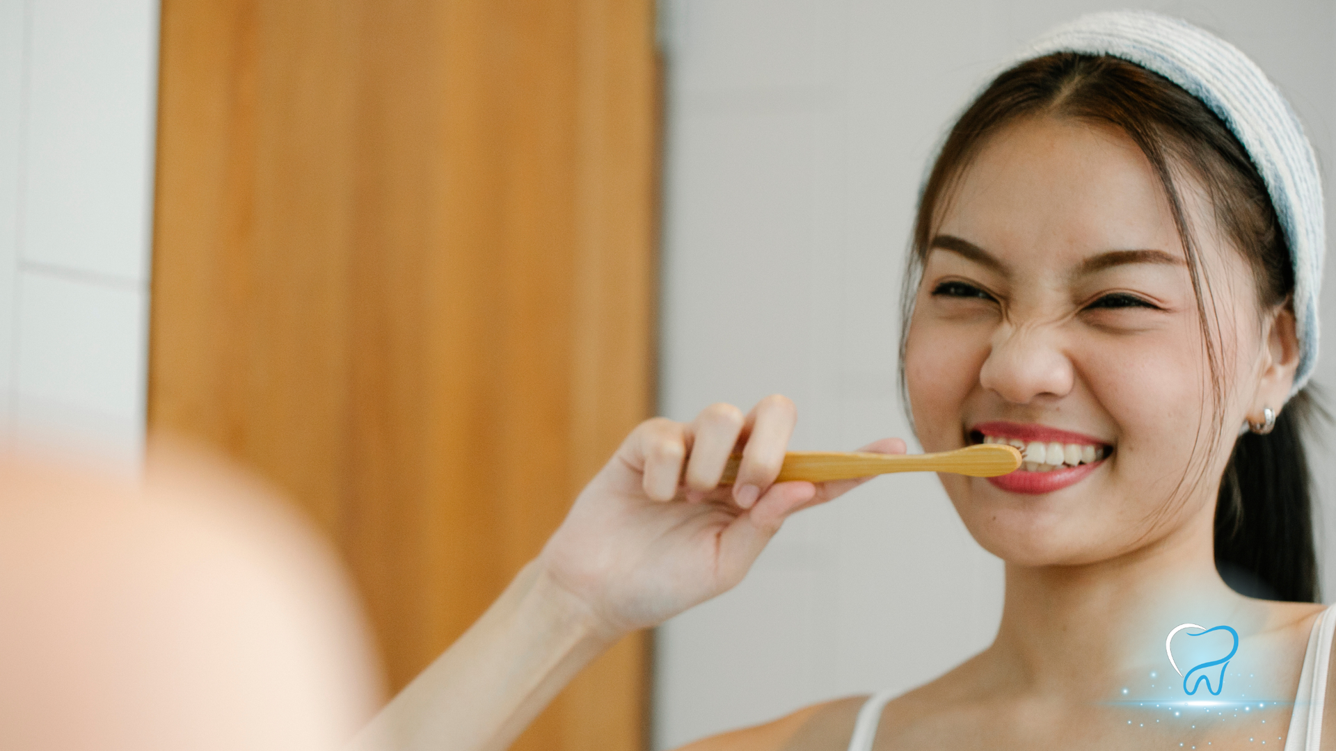 Person brushing teeth and smiling in a bathroom mirror.