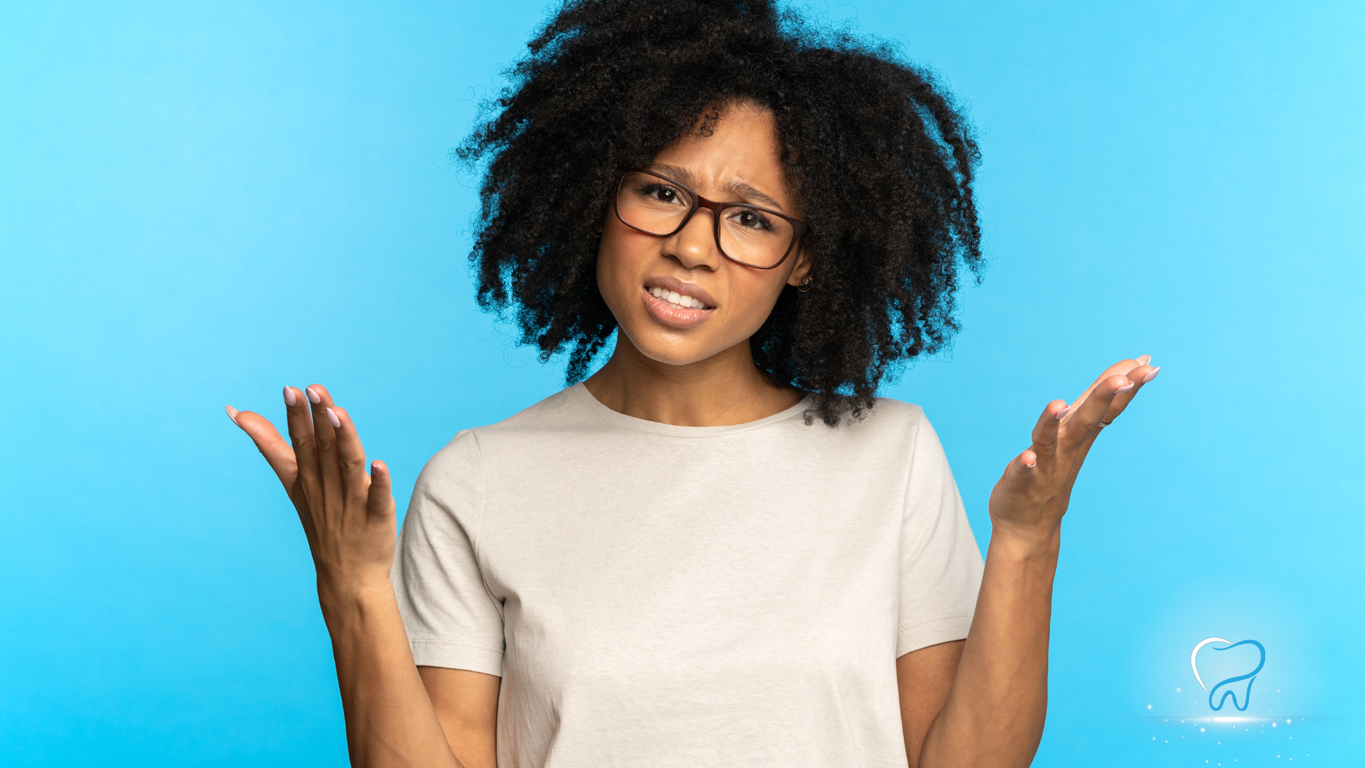 Woman with curly hair and glasses shrugging against a blue background