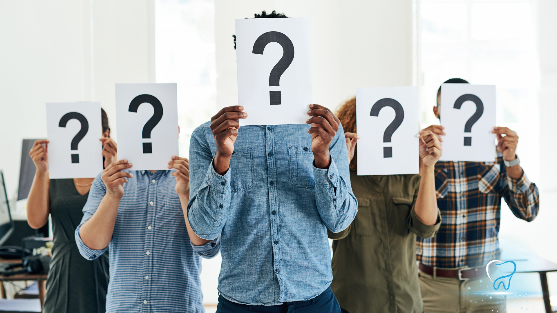 Group of people holding question mark signs in an office, hiding their faces behind the symbols.