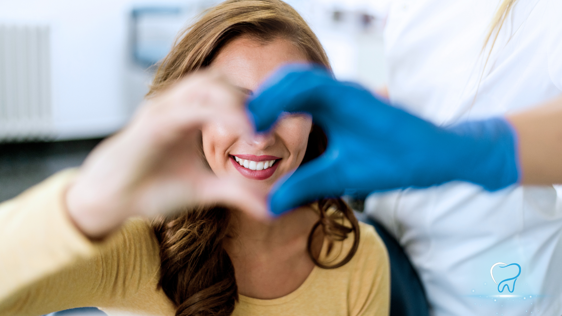Woman smiling as gloved hands frame a heart shape in a bright clinic setting