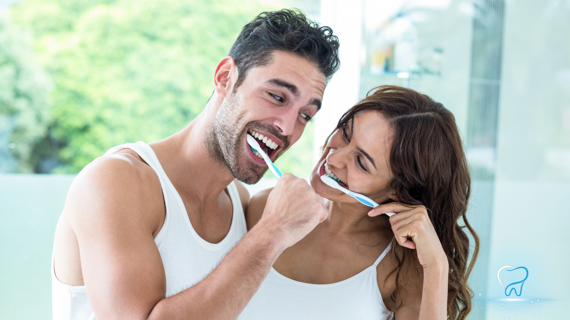 Couple brushing their teeth together in a bright bathroom, smiling playfully at each other.