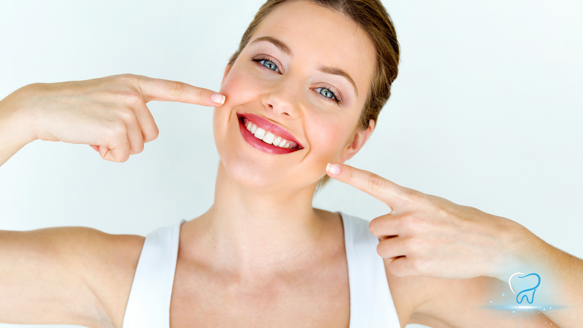 Smiling woman in a white top pointing to her cheeks against a bright background