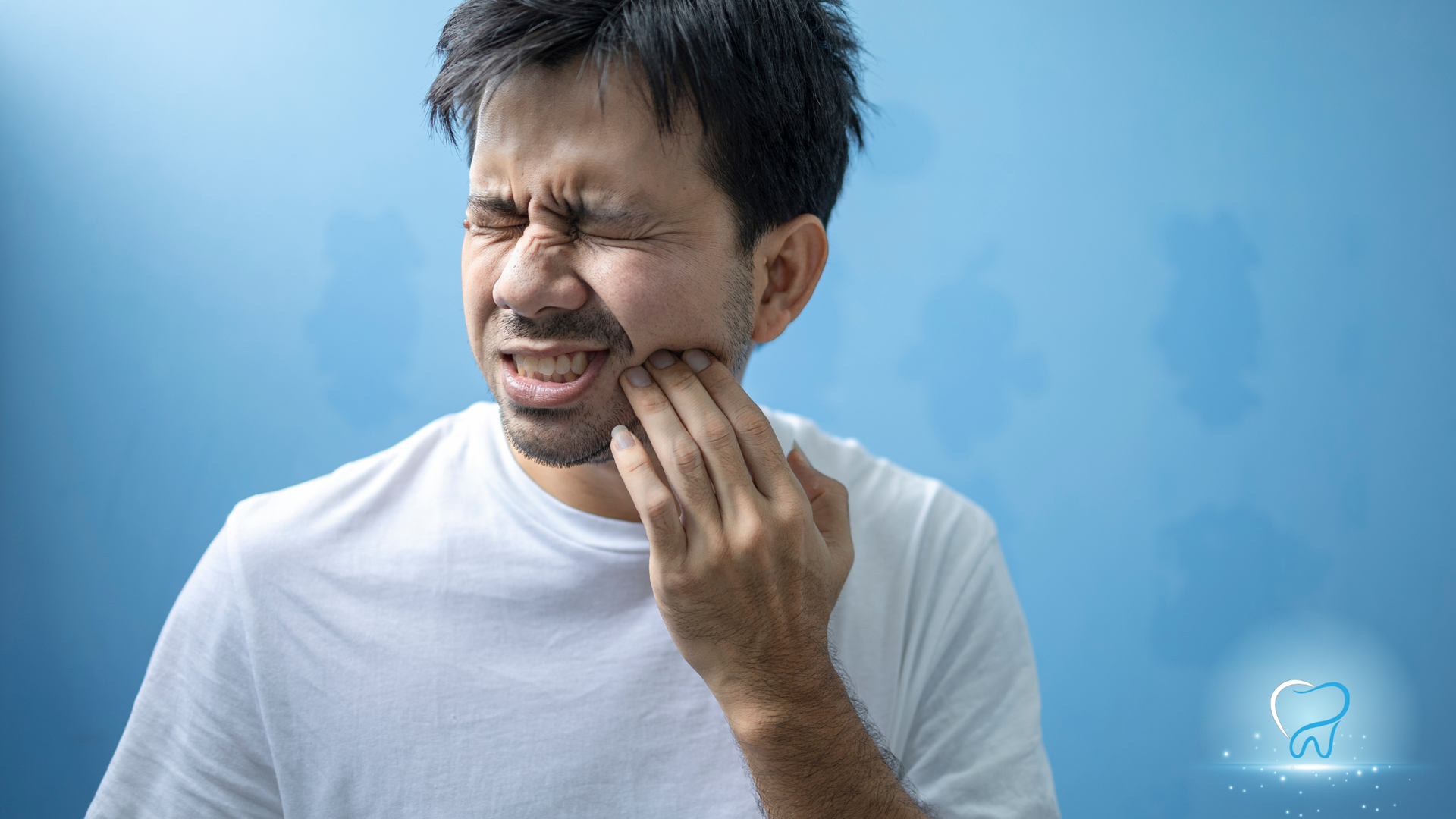 Man grimacing and holding his cheek, appearing to have tooth pain against a blue background