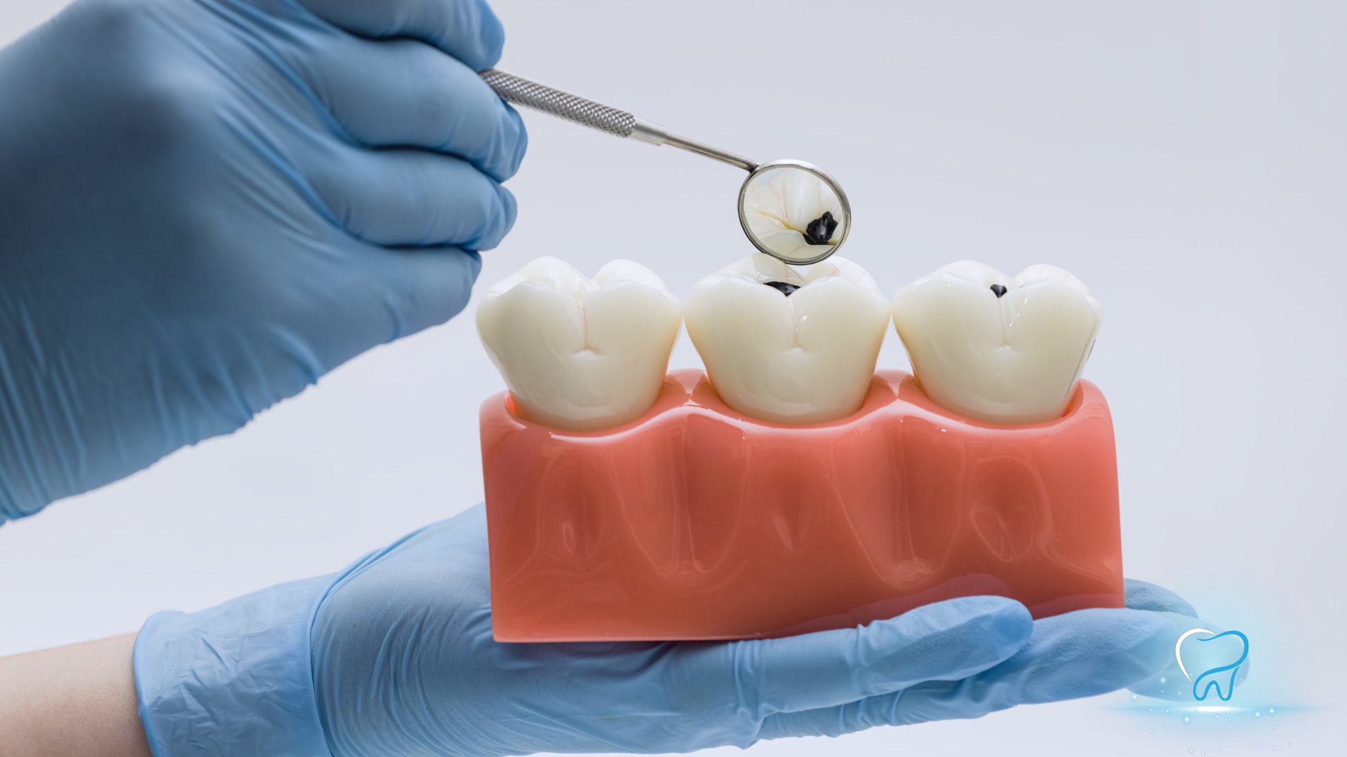 Gloved hand using a dental tool to clean a tooth model on pink gums