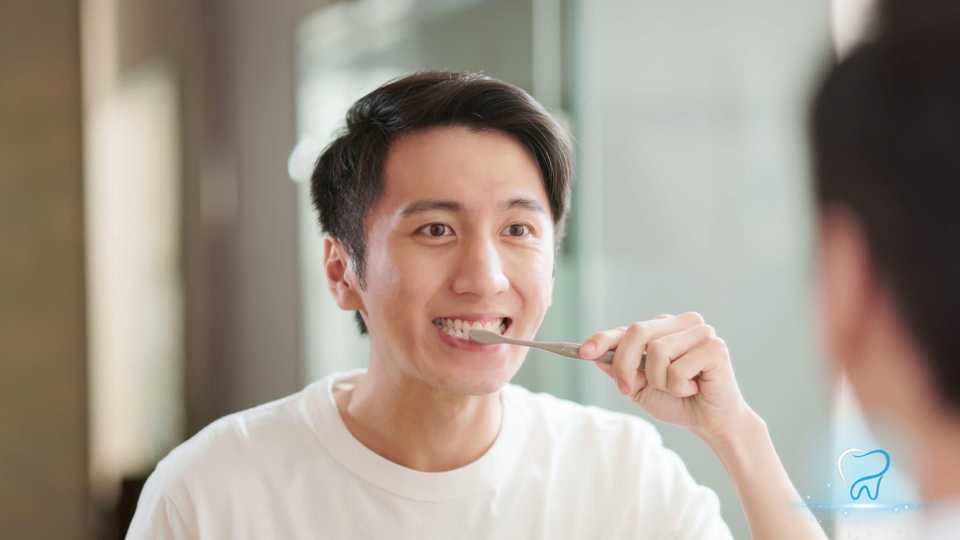 Person brushing teeth while looking in a mirror, smiling in a bright bathroom.