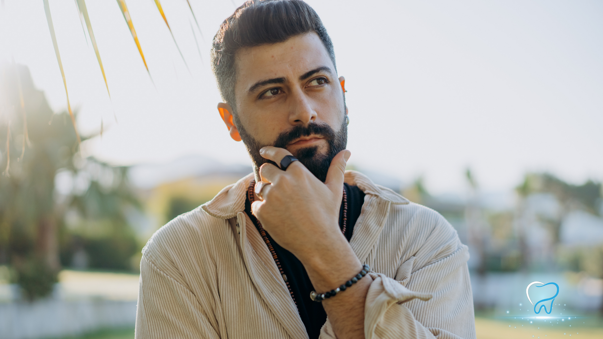 Thoughtful man with a beard resting his chin on his hand outdoors in soft sunlight
