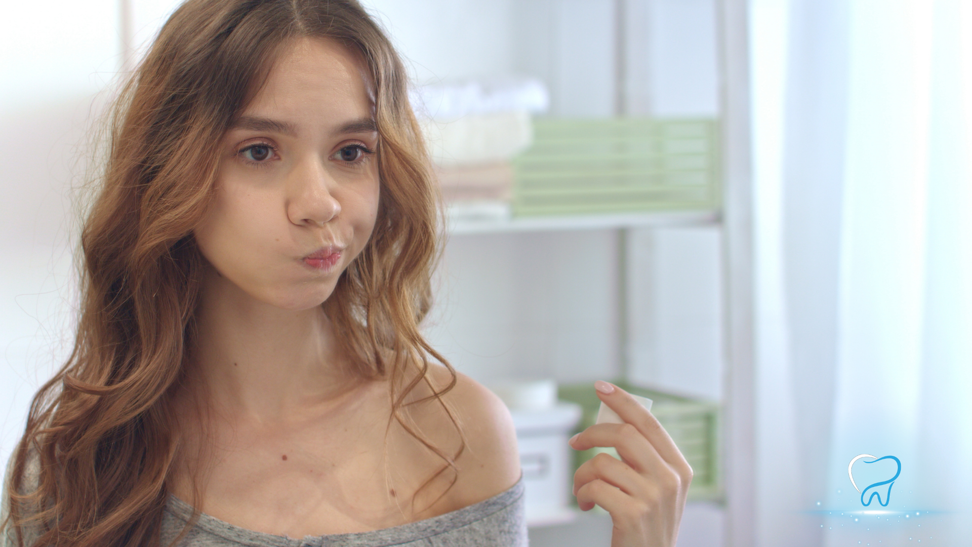 Young woman with wavy hair making a pout, standing indoors by a bright window.