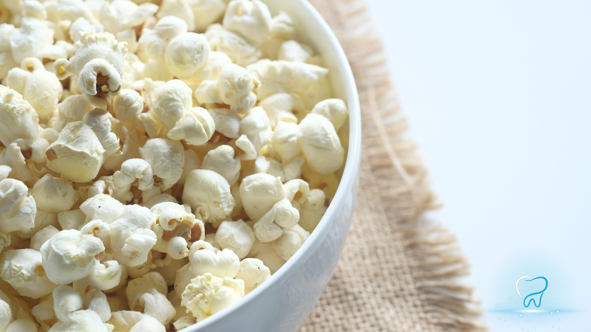 White bowl filled with popcorn on a burlap cloth, with a light blue background