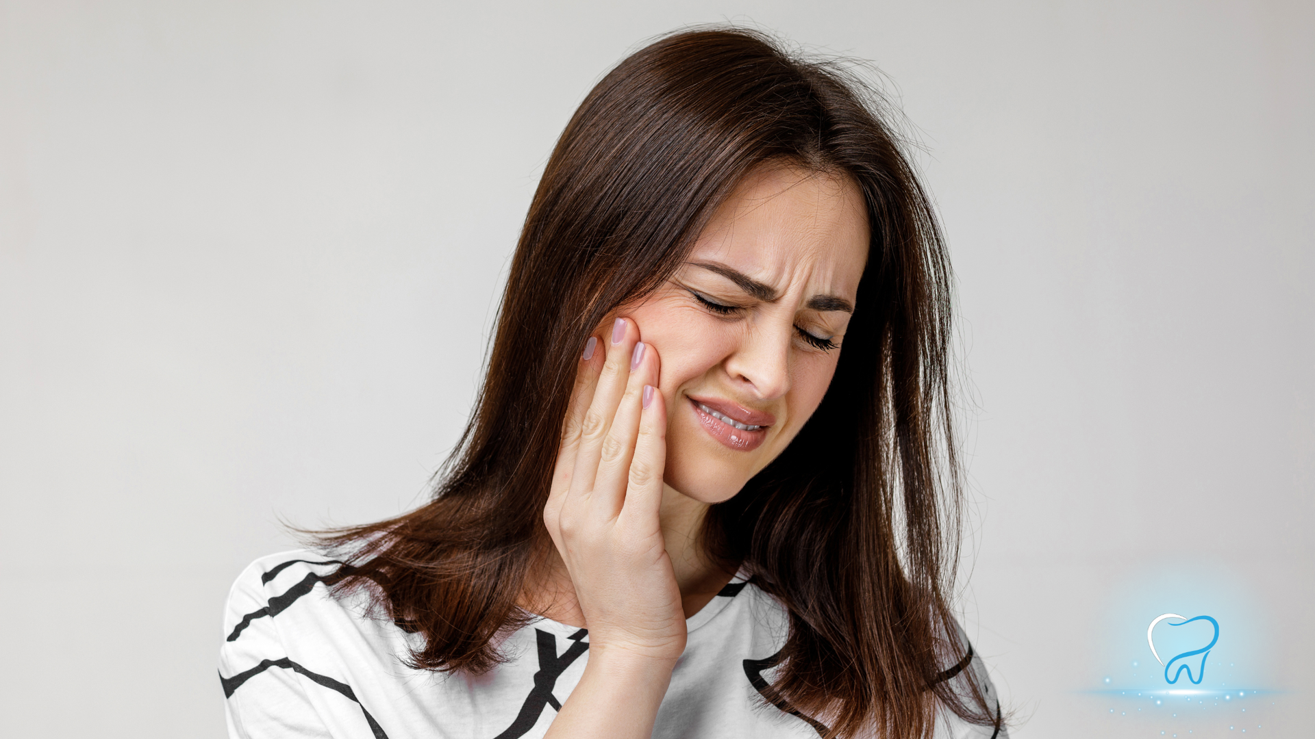 Woman holding her cheek with a pained expression, suggesting tooth pain.