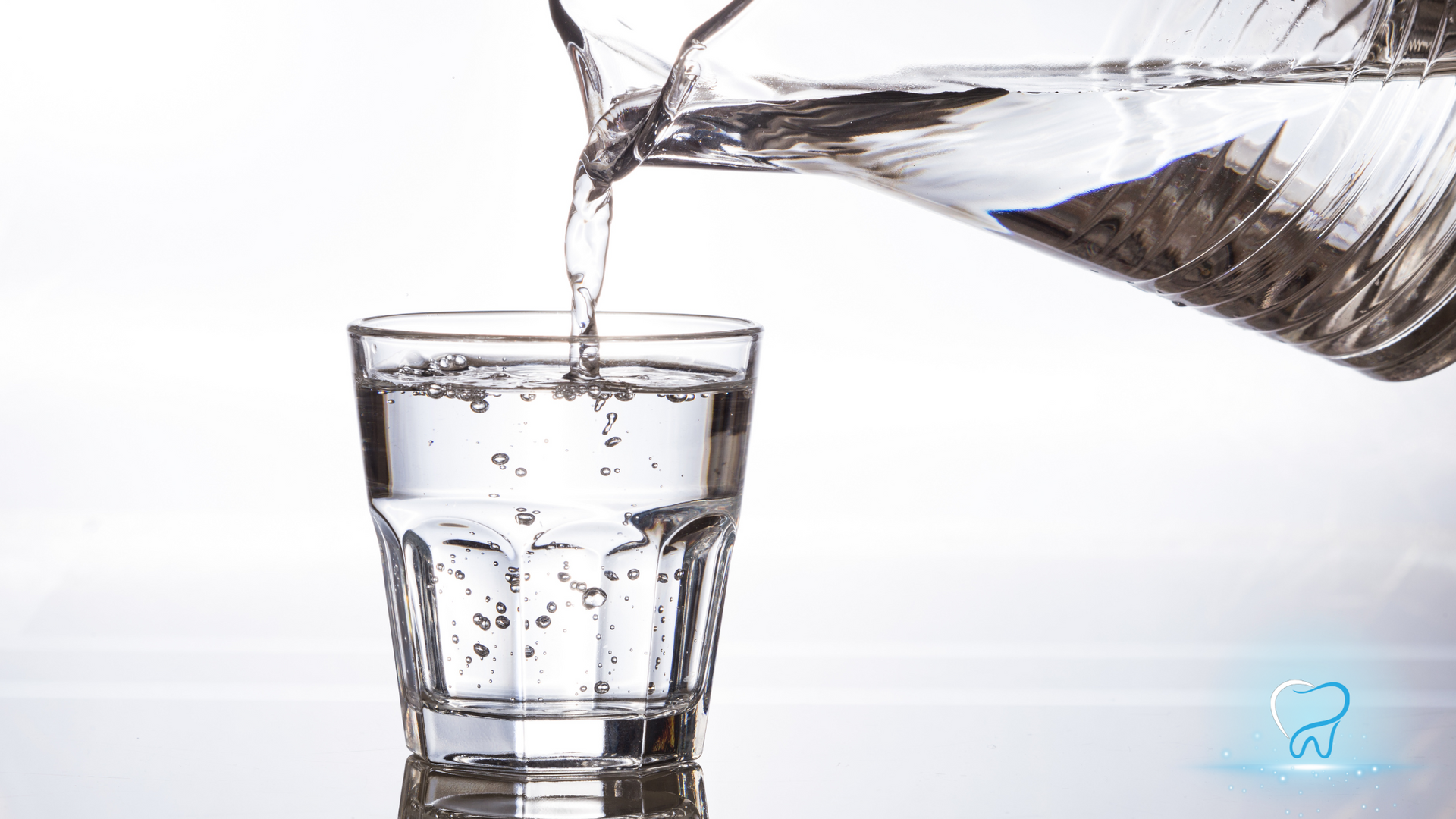 Water being poured from a pitcher into a clear glass on a white background.