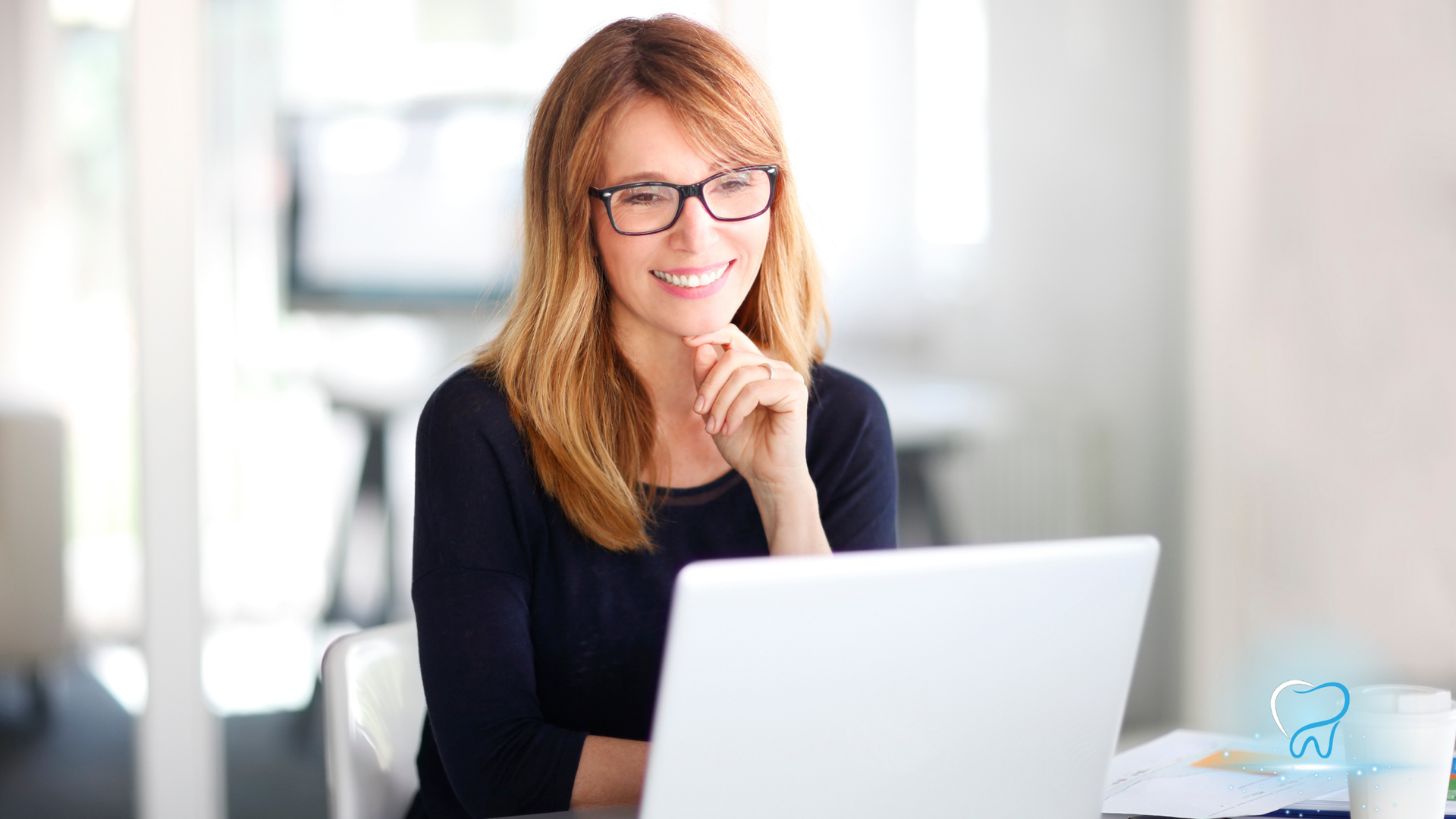 Smiling person with glasses using a laptop in a bright office