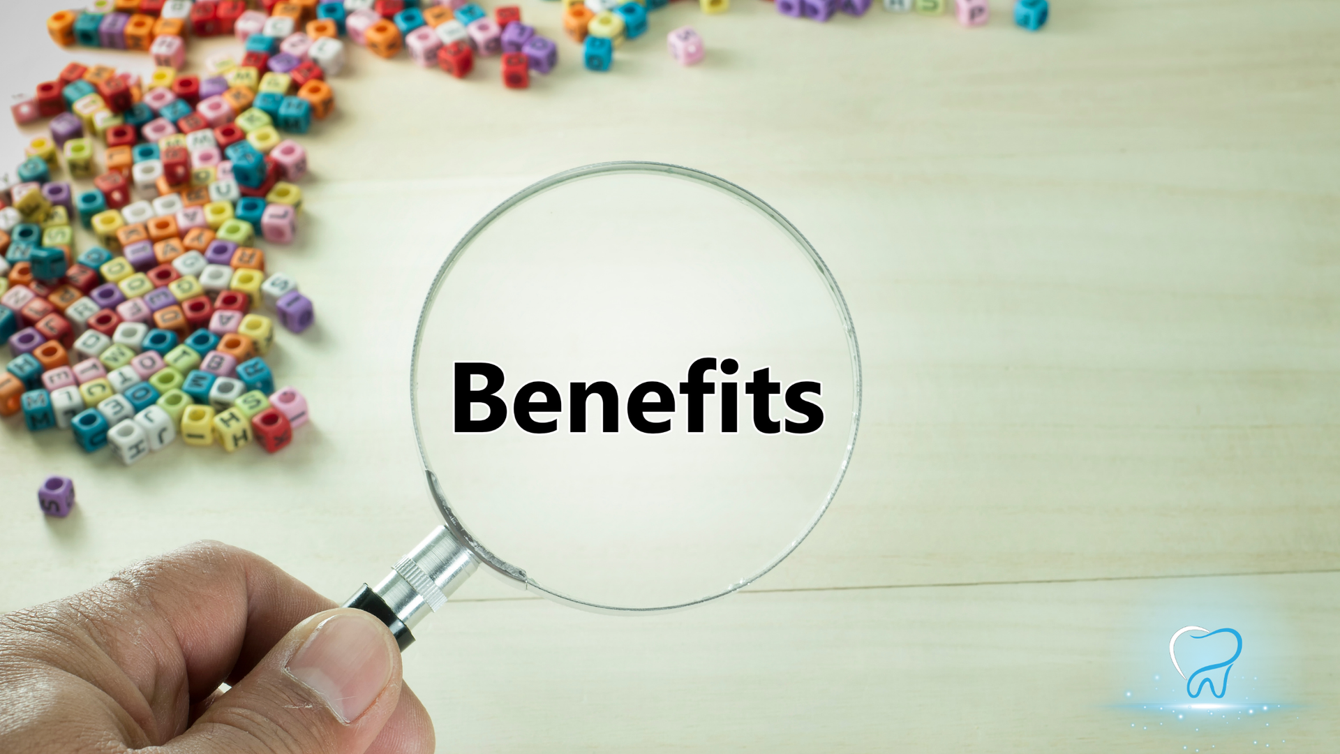 Magnifying glass over the word “Benefits” with colorful letter tiles scattered on a light wooden surface