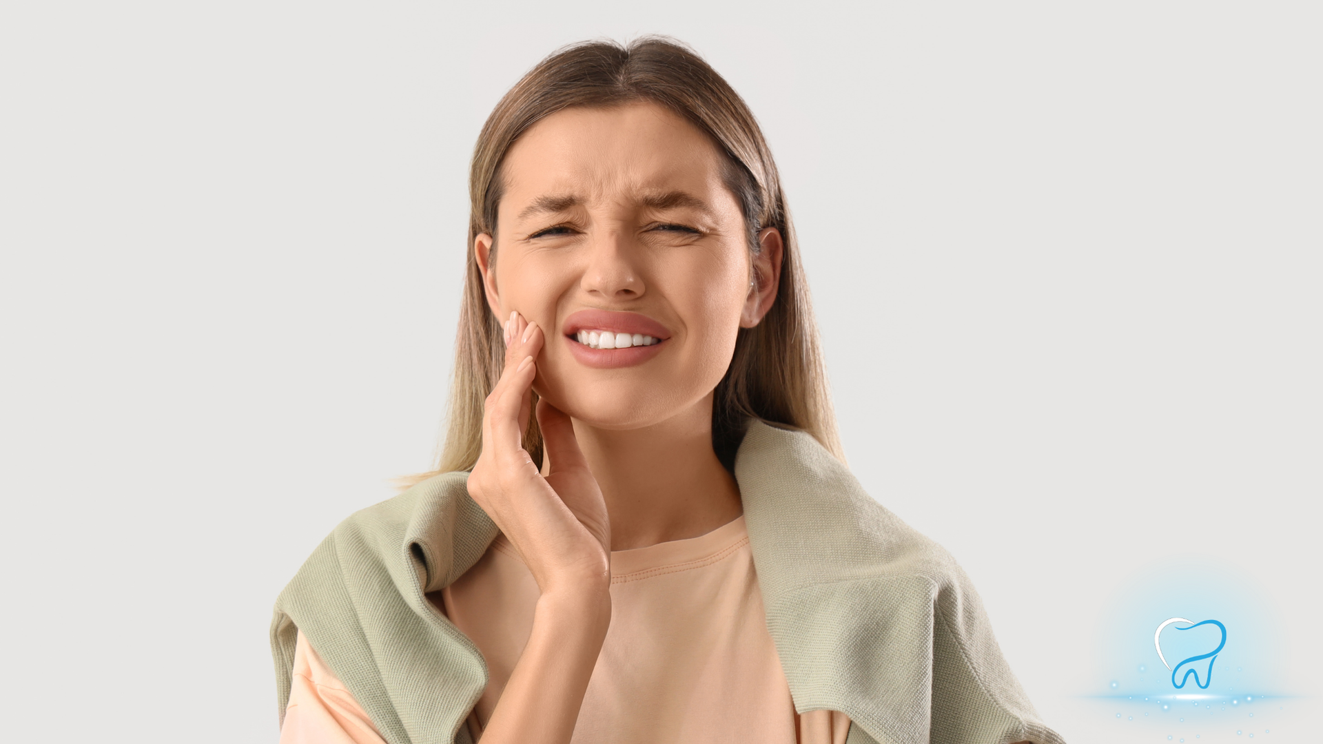 Woman pressing her cheek with a pained expression, suggesting tooth or jaw pain, against a light background.